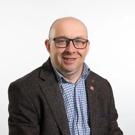 Councillor Stuart Allen wearing a dark grey jacket and a blue and white checked shirt smiling