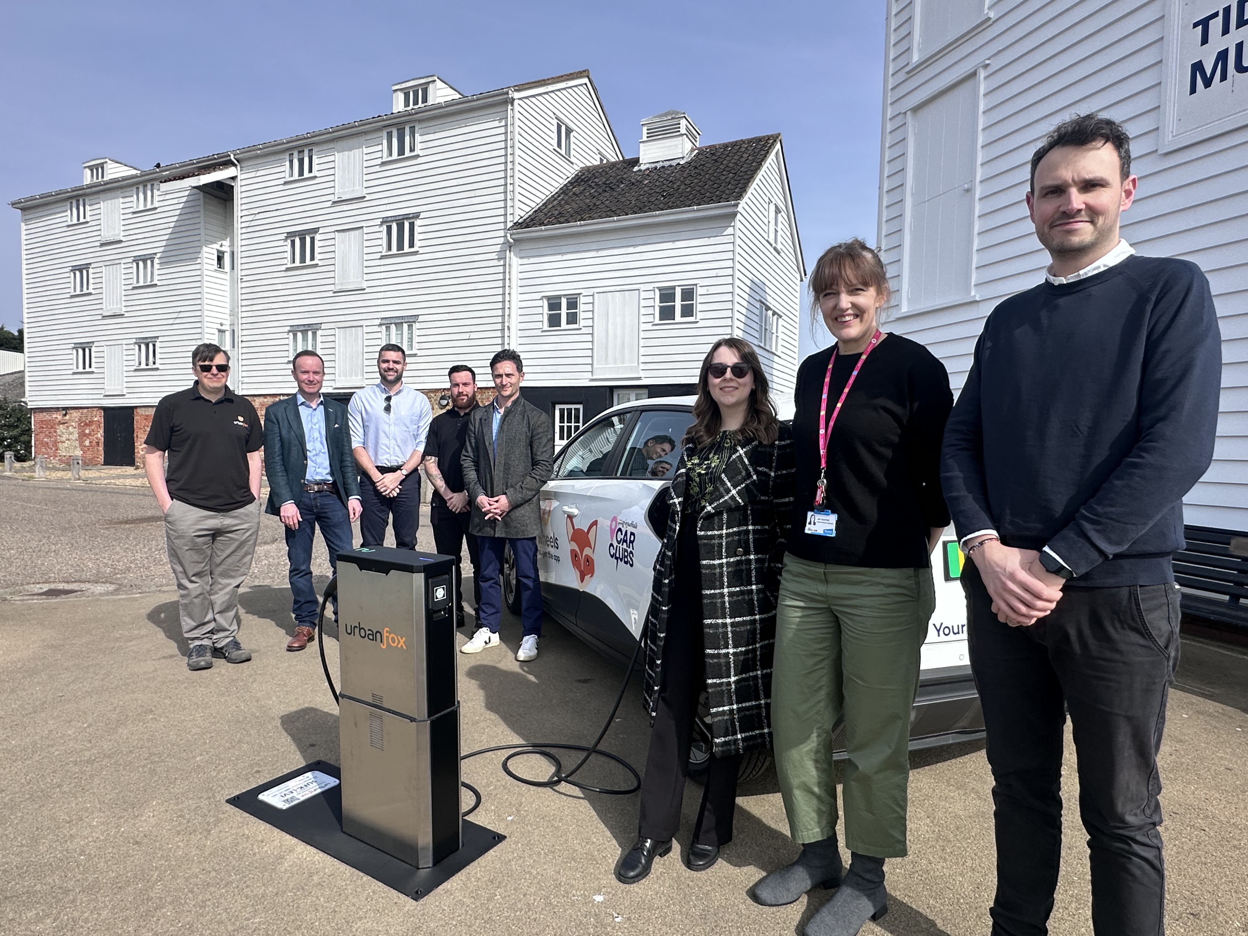 eight people stand next to an electric vehicle and charging point in front of the Tide Mill in Woodbridge