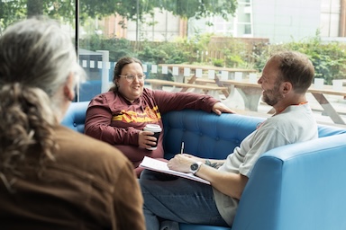 Three people having a drink in a cafe. Two are facing the camera. One is facing away. 