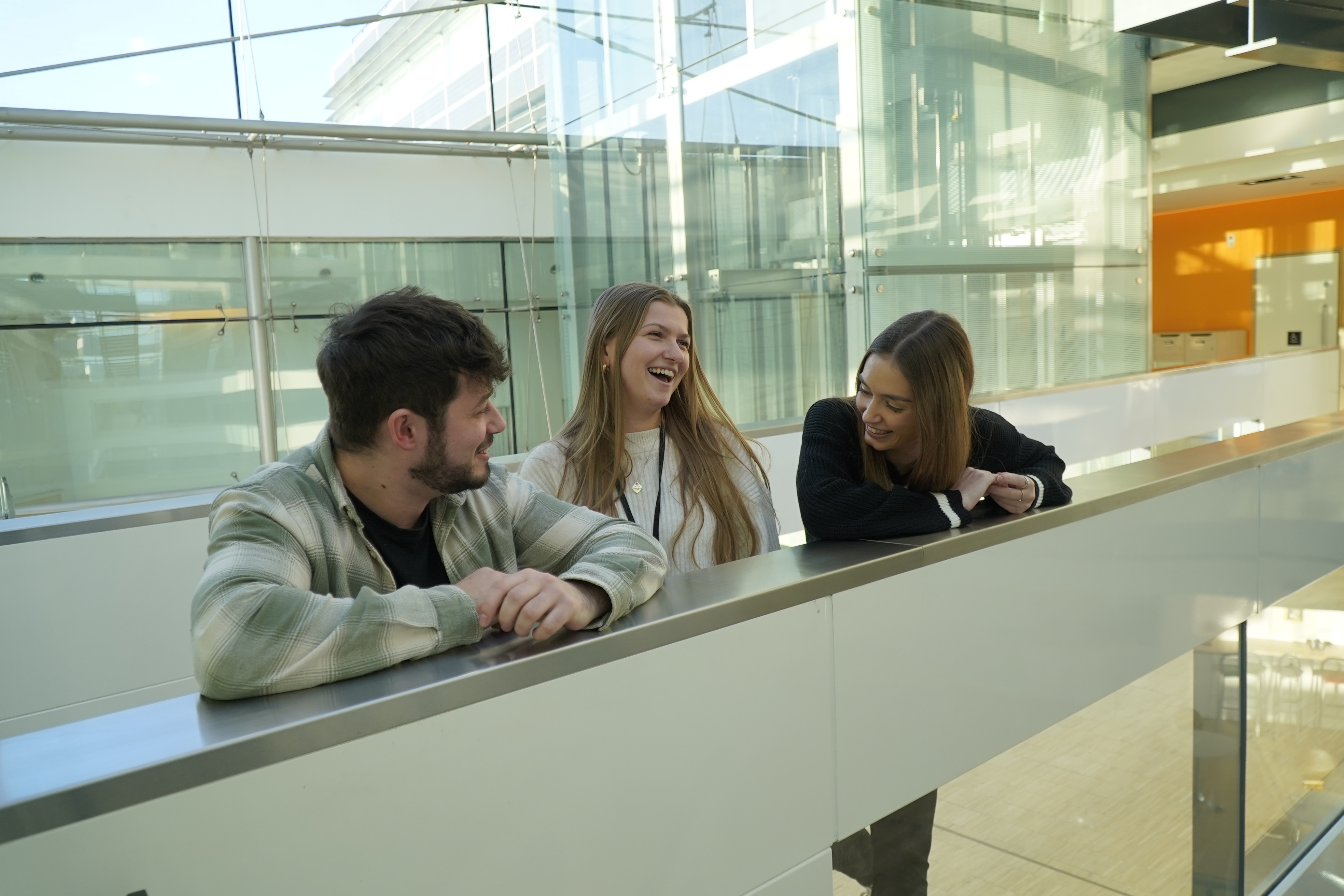 Three young people standing on a balcony laughing. 