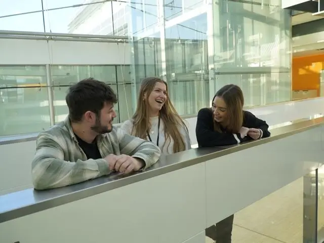 Three young people standing on a balcony laughing. 