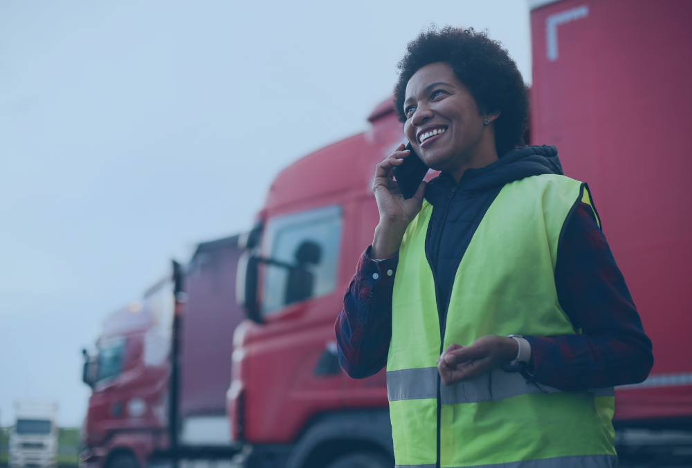 A person in high visability jacket, on a mobile phone, standing in front of two red lorries. 