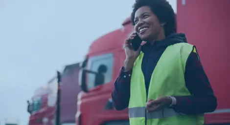 A person in high visability jacket, on a mobile phone, standing in front of two red lorries.