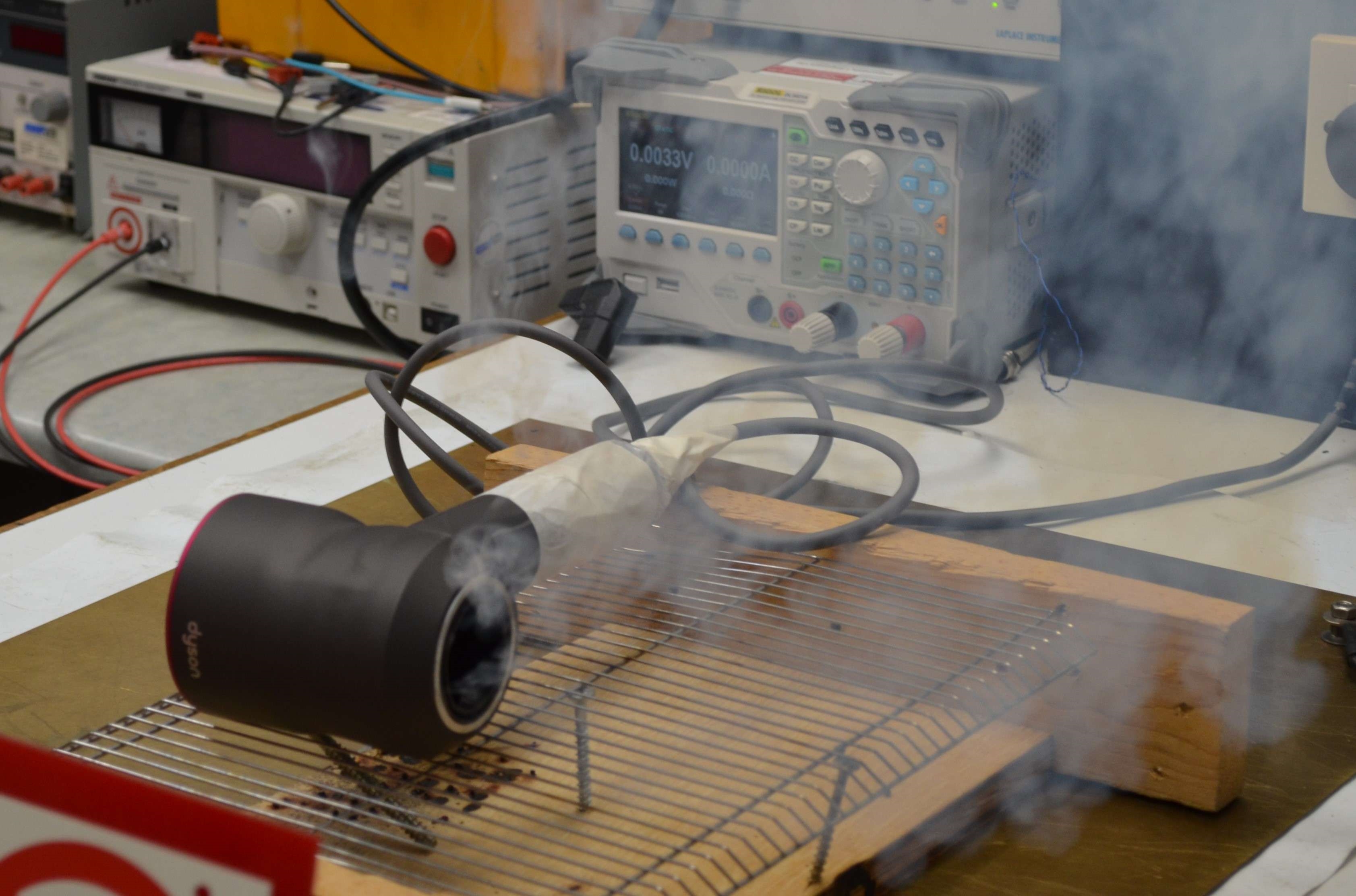 A counterfeit Dyson ‘Supersonic’ hairdryer on a metal rack emitting smoke during testing