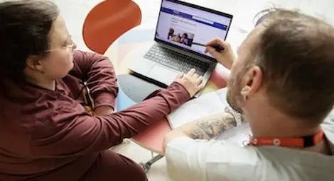 Two people looking at a laptop with the Adult Social Care pages open.