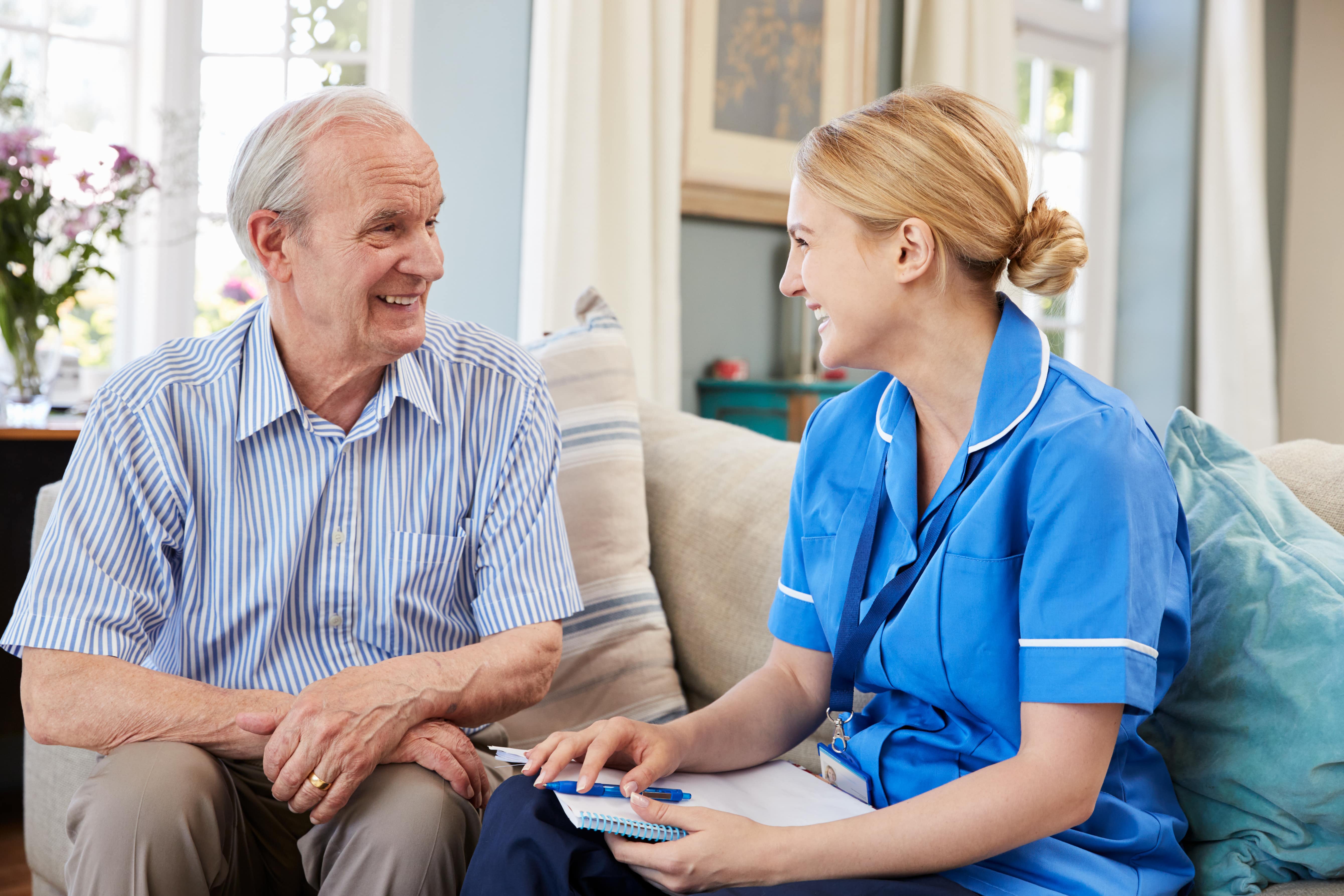 Older man sitting on a sofa with his carer going through paperwork