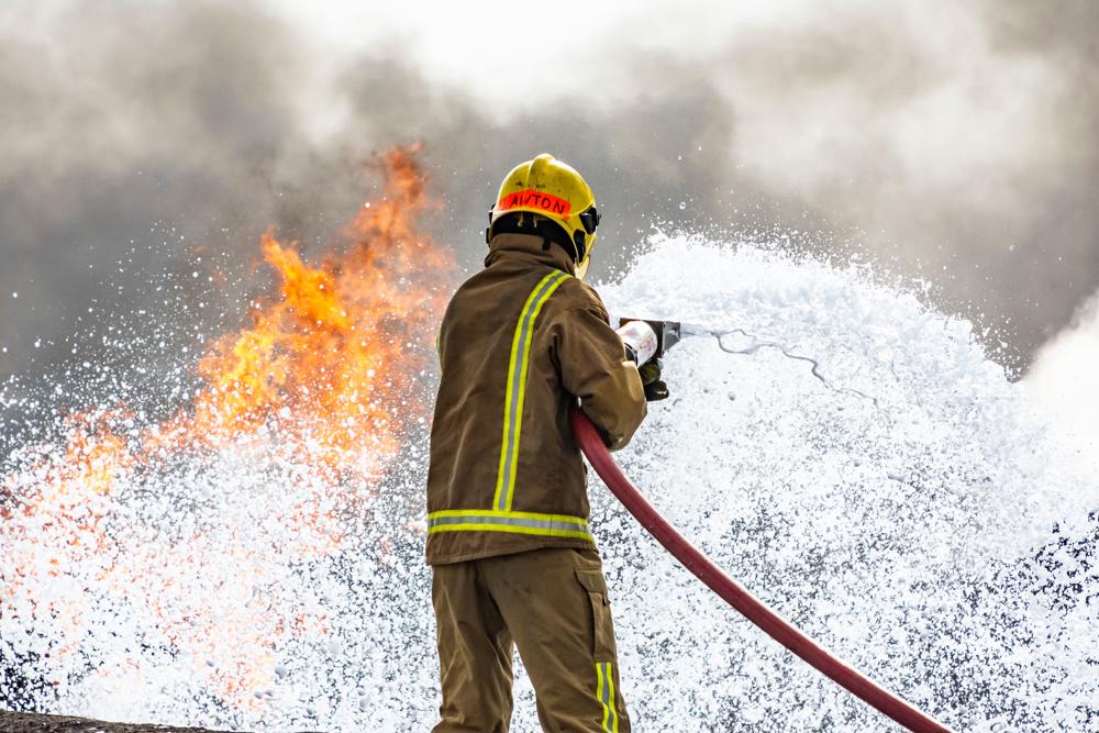 Firefighter uses water to tackle a fire, smoke can also be seen