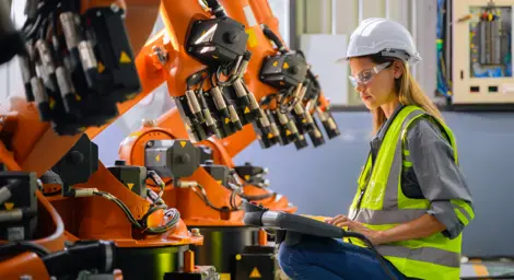 A woman is wearing personal protective equipment and working with large orange coloured machinery.