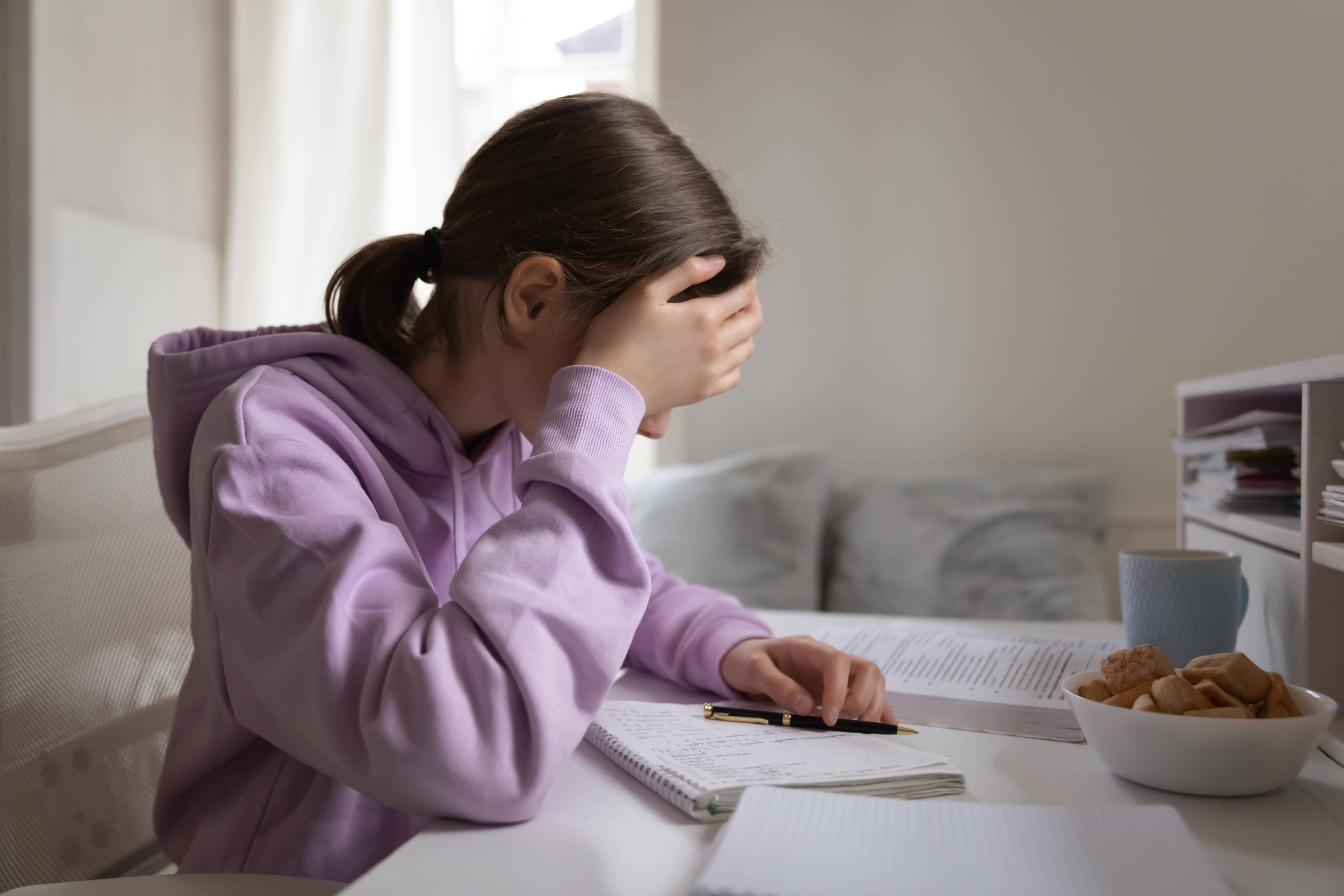 Young school girl holding head and writing in journal, feeling anxious and sad