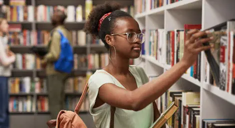 Young student picks out book in library